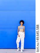 Full body of fit African American female in bra and overall looking away while standing on blue background in city. Black woman in bra near blue wall. Стоковое фото, агентство Ingram Publishing / Фотобанк Лори