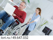 disabled man watching movie on laptop while cleaner is working. Стоковое фото, агентство Ingram Publishing / Фотобанк Лори