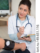 female doctor writing on clipboard while checking blood pressure. Стоковое фото, агентство Ingram Publishing / Фотобанк Лори