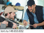 apprentice being advised how to apply caulk to window. Стоковое фото, агентство Ingram Publishing / Фотобанк Лори