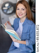 beautiful young woman reading book at laundromat. Стоковое фото, агентство Ingram Publishing / Фотобанк Лори