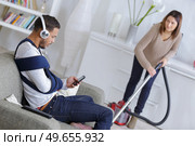 woman vacuuming while man is resting on a couch. Стоковое фото, агентство Ingram Publishing / Фотобанк Лори