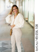 Positive young blond haired female in smart casual outfit smiling and looking at camera while fixing hair. Smiling woman with sunglasses in beige outfit. Стоковое фото, агентство Ingram Publishing / Фотобанк Лори