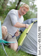 man with hammer pitching tent. Стоковое фото, агентство Ingram Publishing / Фотобанк Лори