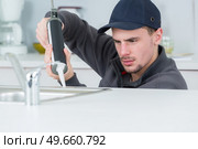 young handyman applying silicone sealant with gun around sink. Стоковое фото, агентство Ingram Publishing / Фотобанк Лори