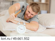 young man tries to break the alarm clock with hammer. Стоковое фото, агентство Ingram Publishing / Фотобанк Лори
