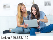 two smiling girlfriends sitting on sofa and doing homework. Стоковое фото, агентство Ingram Publishing / Фотобанк Лори