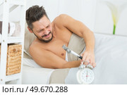 sleepy young man breaking alarm with a hammer. Стоковое фото, агентство Ingram Publishing / Фотобанк Лори