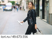 Side view of stylish female in leather pants and jacket carrying bag and takeaway reusable bottle while commuting on town street looking at camera. Smart casual lady with bag and bottle walking on street. Стоковое фото, агентство Ingram Publishing / Фотобанк Лори