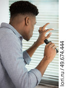 discreet young man looking through window blinds holding binoculars. Стоковое фото, агентство Ingram Publishing / Фотобанк Лори