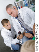 older doctor training young doctor on measuring pressure. Стоковое фото, агентство Ingram Publishing / Фотобанк Лори