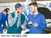 apprentice mechanic with clipboard questioning man using telephone. Стоковое фото, агентство Ingram Publishing / Фотобанк Лори