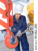 Woman attaching metal wire to hook of crane. Стоковое фото, агентство Ingram Publishing / Фотобанк Лори