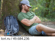 man hiker taking rest sitting at tree in a forest. Стоковое фото, агентство Ingram Publishing / Фотобанк Лори