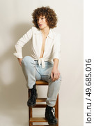 Full body of thoughtful female model with curly red hair in casual outfit chilling on wooden stool and looking away against white background. Pensive woman relaxing on ladder. Стоковое фото, агентство Ingram Publishing / Фотобанк Лори