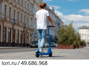 A man is riding a blue scooter down a city street. Стоковое AI-изображение, AI-художник Ярославский Максим / Фотобанк Лори