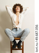 Full length of bossy female model with red hair, in stylish clothes resting on wooden stool with hands on head and staring at camera against white wall. Arrogant woman chilling on chair. Стоковое фото, агентство Ingram Publishing / Фотобанк Лори