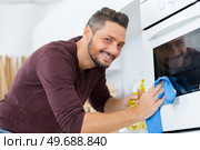happy man cleaning oven with rag and bottle spray. Стоковое фото, агентство Ingram Publishing / Фотобанк Лори