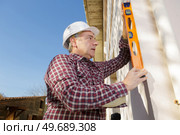 Man using spirit level on exterior wall. Стоковое фото, агентство Ingram Publishing / Фотобанк Лори
