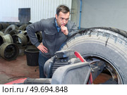 mechanic looking pensively at large tyre. Стоковое фото, агентство Ingram Publishing / Фотобанк Лори