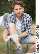 wounded man bandaging leg while on camping. Стоковое фото, агентство Ingram Publishing / Фотобанк Лори
