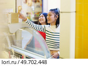 Positive young Asian girlfriends smiling happily while purchasing together ice cream in shop. Happy Asian woman buying ice cream. Стоковое фото, агентство Ingram Publishing / Фотобанк Лори