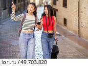 Two young Chinese women passing by guided by the GPS of their smartphone, through the streets of Granada, Spain. Concept of Asian people traveling in Europe.. Asian female travelers pointing away while walking on street. Стоковое фото, агентство Ingram Publishing / Фотобанк Лори