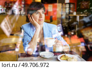 Pondering woman in stylish blue jacket sitting at table with cup of hot drink and looking away during breakfast in cafe. Wistful lady drinking coffee in cafeteria. Стоковое фото, агентство Ingram Publishing / Фотобанк Лори
