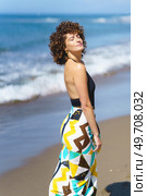 Calm lady in colorful swimwear with closed eyes standing on sandy beach near waving sea during summer holidays. Serene female tourist standing against sea on sunny day. Стоковое фото, агентство Ingram Publishing / Фотобанк Лори