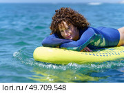 Side view portrait of young female surfer in wetsuit with curly hair relaxing on paddleboard floating on sea water during summer vacation. Smiling woman lying on SUP board in sea. Стоковое фото, агентство Ingram Publishing / Фотобанк Лори
