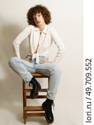 Full body of self-confident woman, with curly red hair in casual outfit chilling on wooden stool and looking away against white background. Self-confident woman relaxing on ladder. Стоковое фото, агентство Ingram Publishing / Фотобанк Лори