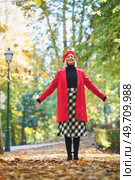 Full body of smiling female wearing elegant clothes spreading arms and throwing dry leaves on footpath in autumn park. Happy woman throwing dry leaves in park. Стоковое фото, агентство Ingram Publishing / Фотобанк Лори