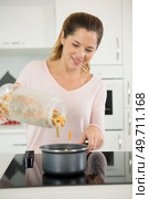 smiling young woman adding pasra to pot. Стоковое фото, агентство Ingram Publishing / Фотобанк Лори