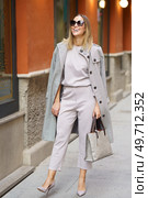 Full length of positive female in formal outfit and coat wearing sunglasses and coat standing on paved sidewalk and admiring view of old building. Cheerful woman in stylish outfit standing on street. Стоковое фото, агентство Ingram Publishing / Фотобанк Лори
