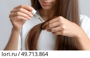 Woman applying hair treatment to her long hair with a dropper in a bright room. Женщина наносит средство для волос на свои длинные волосы с помощью пипетки в светлой комнате. Стоковое AI-изображение, AI-художник Katsiaryna Repich / Фотобанк Лори