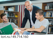 young man reading a book while the teacher is observing. Стоковое фото, агентство Ingram Publishing / Фотобанк Лори