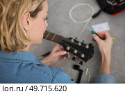 over the shoulder view of woman restringing a guitar. Стоковое фото, агентство Ingram Publishing / Фотобанк Лори
