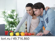 a couple cooking at kitchen and using laptop. Стоковое фото, агентство Ingram Publishing / Фотобанк Лори