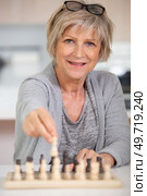 cheerful senior woman moves piece on chess board. Стоковое фото, агентство Ingram Publishing / Фотобанк Лори