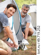 two middle-aged men erecting tents in the countryside. Стоковое фото, агентство Ingram Publishing / Фотобанк Лори