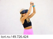 Young fit woman in VR goggles playing videogame while raising arms over head with invisible object against white background. Sportswoman in VR headset raising hands while playing videogame. Стоковое фото, агентство Ingram Publishing / Фотобанк Лори