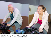 senior man and young lady on static cycle machines. Стоковое фото, агентство Ingram Publishing / Фотобанк Лори