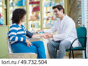 Side view of happy male druggist measuring blood pressure of woman while sitting with client and looking at each other in pharmacy. Cheerful druggist and woman customer in pharmacy. Стоковое фото, агентство Ingram Publishing / Фотобанк Лори