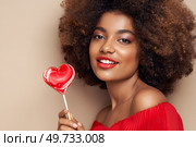 Beautiful portrait of an African girl with a heart shaped lollipop. Valentine’s Day. Symbol of love. Стоковое фото, агентство Ingram Publishing / Фотобанк Лори
