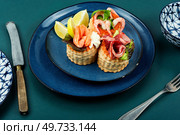 Puff pastry tartlets or canapes with fish, shrimp and bacon on a plate on the table.. Tartlets with seafood and bacon, tasty snack. Стоковое фото, агентство Ingram Publishing / Фотобанк Лори