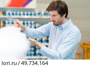 handsome concentrated young man choosing paints in hardware store. Стоковое фото, агентство Ingram Publishing / Фотобанк Лори