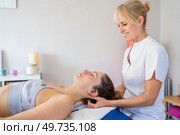 Side view of smiling female blond hair physiotherapist rubbing neck of client lying face up in bed and closing eyes during massage treatment. Cheerful female osteopath treating patient in hospital. Стоковое фото, агентство Ingram Publishing / Фотобанк Лори