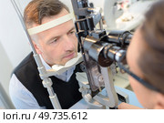 optometrist in exam room with man in chair. Стоковое фото, агентство Ingram Publishing / Фотобанк Лори