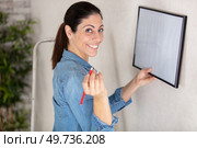 young woman putting photo frame on white wall. Стоковое фото, агентство Ingram Publishing / Фотобанк Лори