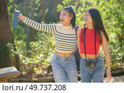 Cheerful young Asian female friends in casual apparel, standing in green forest of Alhambra and pointing away while enjoying picturesque views during summer trip in Granada. Happy Asian women pointing away and showing route in forest. Стоковое фото, агентство Ingram Publishing / Фотобанк Лори